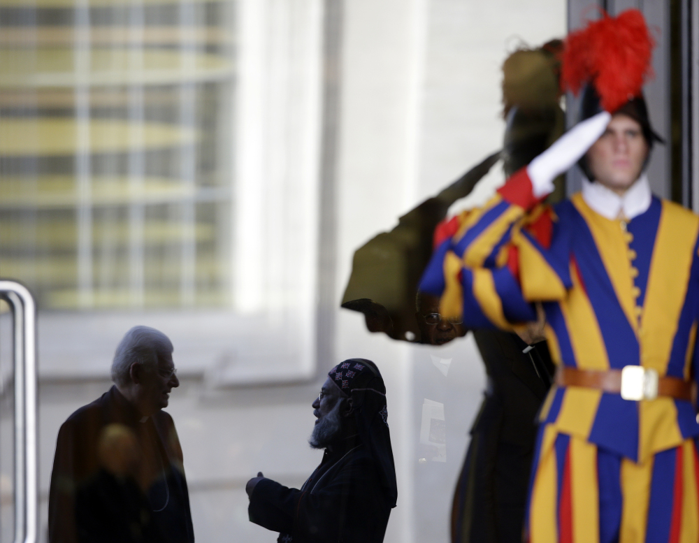 Cardinal Angelo Scola, left, and Cardinal Baselios Cleemis,  are reflected on the glass door of the Paul VI hall as they arrive for a morning session of a two-week synod on family issues at the Vatican, Tuesday.