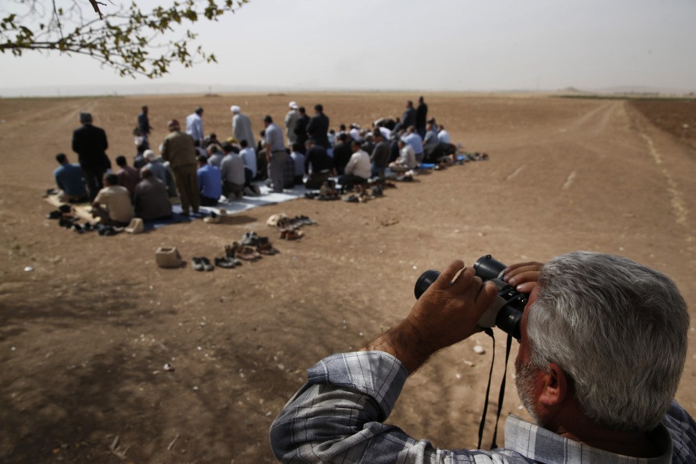 In this  Friday, Oct. 10, 2014 file  photo, a Turkish Kurd, standing in Mursitpinar,Turkey, on the Turkey-Syria border, uses binoculars to watch intensified fighting over the border in Kobani, Syria, between Syrian Kurds and the militants of Islamic State group, as Turkish Kurds offer their Muslim Friday prayers.