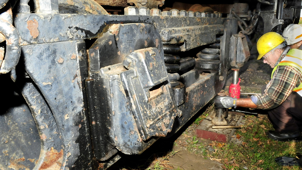 Ron Jenkins, of New England Steam Corp., jacks a wheel on a coal tender car Monday behind the Old 470 steam locomotive in Waterville.
