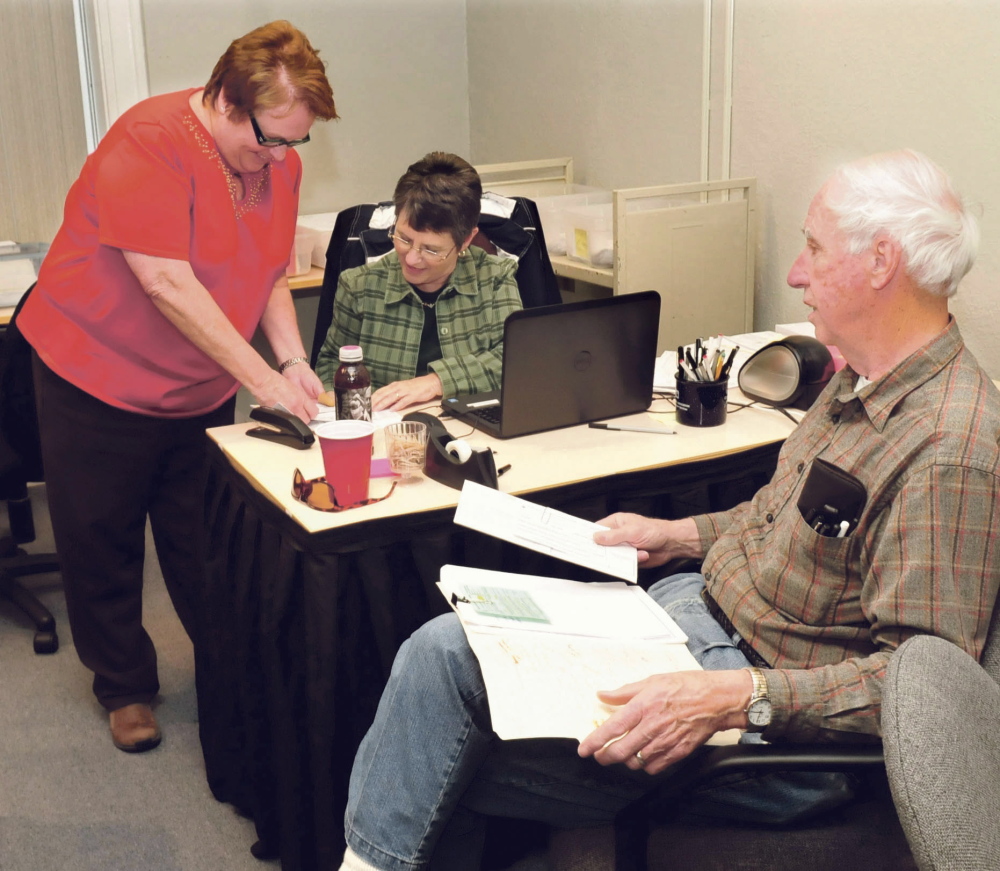 Waterville assistant city clerks Arlene Strahan, left, and Patricia Loisel confer after Gil Pelletier brought in absentee ballots he collected from residents on Monday.