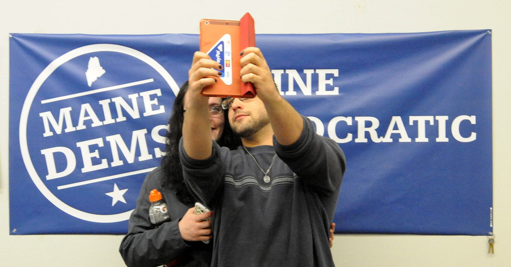 Joel Bouchard, 31, right, and Sarah Bailey, 21, both of Winslow, take selfies in front of the sign at the Democratic Party headquarters on Main Street in Waterville on Tuesday night while awaiting election results.