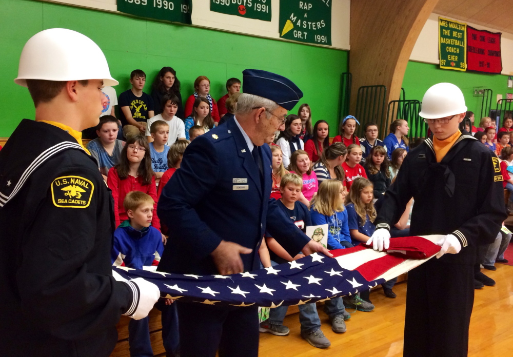 Robert Demchak, 67, of Madison, a retired Air Force veteran, helps Trevor Edes, right, 16, of Anson, and Jonathen Jackson, also 16, of Solon, fold an American flag during a Veterans Day celebration at the Athens Community School on Friday. Edes and Jackson are members of the U.S. Naval Sea Cadets Corps, a youth program that models itself after the training and curriculum of the American military.