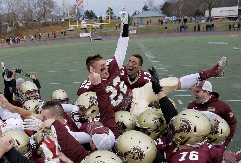 Thornton Academy’s CJ Michaud, 22, and Corey Hart, 13, celebrate with teammates after the Trojans beat Windham in the Class A football state championship at Fitzpatrick Stadium, on Saturday.