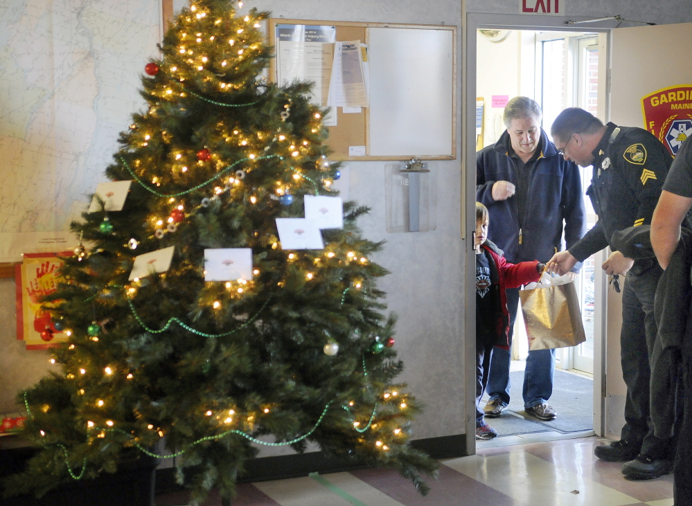 Carson Brigman, 7, and his grandfather, Mike Stoddard, hand Gardiner Police Sgt. Stacy Blair Thursday a bag of presents at the city’s fire station. The duo were presenting public servants gift bags on Christmas that were prepared by their church, Pathway Vineyard.