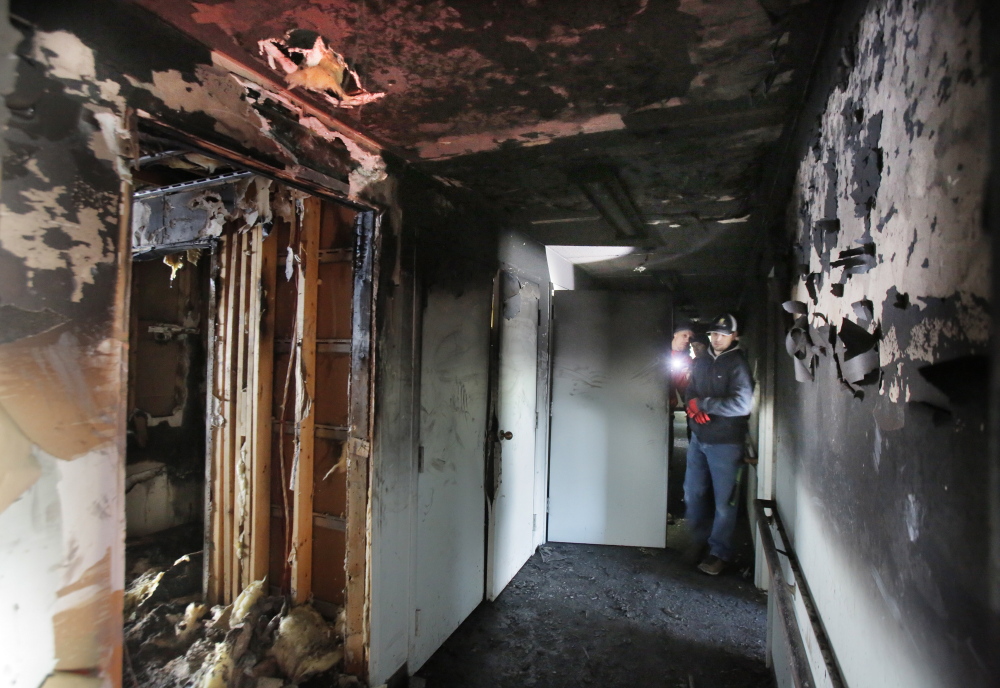 Workers survey damage in a hall at Centennial Place. Kevin Gerrish, property manager for Alpha Management, the building’s owner, said one first-floor apartment was destroyed but the others can be cleaned.