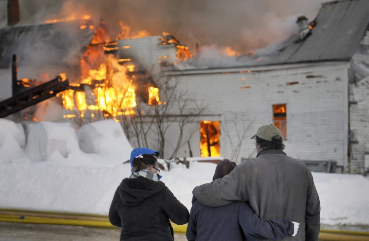 Mark Fenderson, right, is comforted Tuesday while watching his farm burn in Whitefield.  Flames spread from the barn throughout the dairy farm.