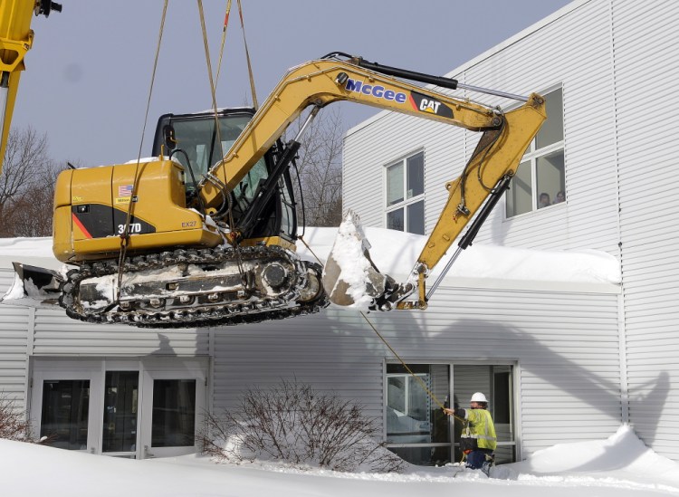 Scott McGee guides an excavator hoisted by a crane Wednesday into a courtyard within Gardiner Area High School. McGee Construction assisted the Gardiner Water District and school with locating and repairing a water main that ruptured. The school was closed to students on Wednesday, but will reopen Thursday.