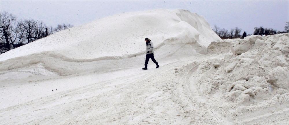 Ryan Baumann walks past the growing pile of snow that has been collected from city streets in Waterville after repeated storms this winter. “That pile is twice the size since I saw it a week ago,” Baumann said. More snow over the long holiday weekend and the continuing work to clear snow from roadsides and intersections could mean the pile will grow still larger.