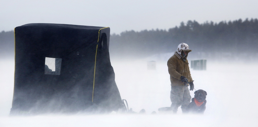 Alan Asselin Jr. of Buxton jigs with his canine companion, Julian, while fishing with his father, Alan Asselin Sr. of Arundel, on Sebago Lake. One of them had to stay inside the shelter at all times so the wind wouldn’t blow it away. Above: The wind sends snow swirling around Greg Symalla of Windham as he digs holes in the ice for fishing with his sons.