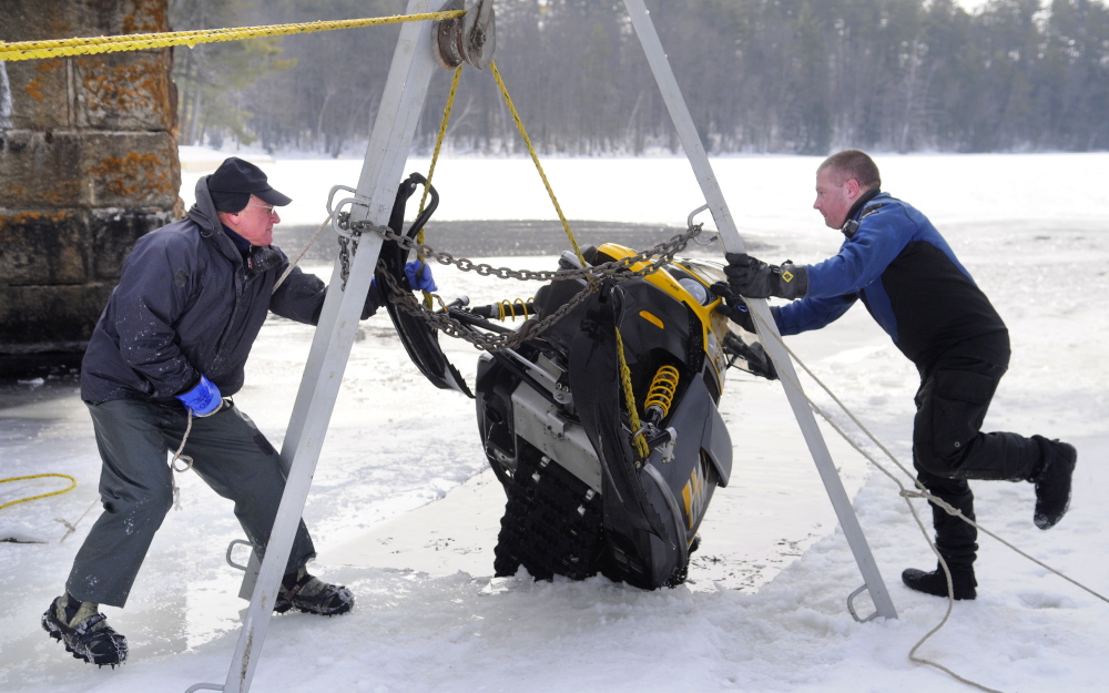 Matt Sinclair, right, and his father, David, secure a snowmobile they hoisted from under the ice on Maranacook Lake in Winthrop on Sunday.