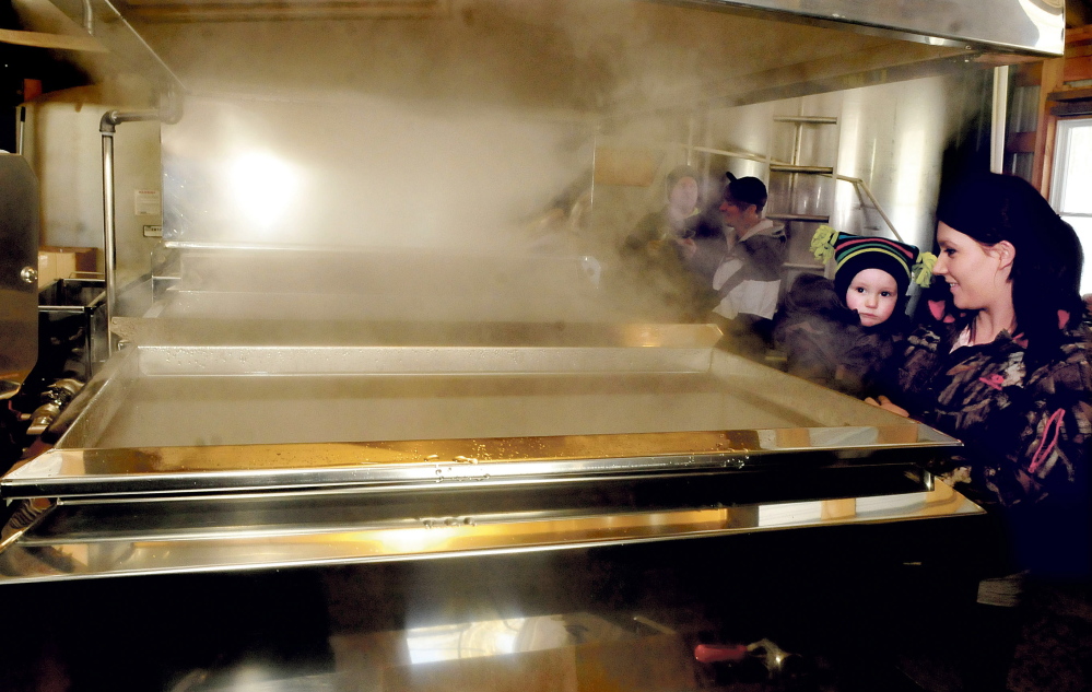 Erika Semones holds her son Samuel on Sunday as they watch smoke rise from an evaporator while sap boils into maple syrup at the Smith Brothers Maple sap house in Skowhegan during Maine Maple Sunday.