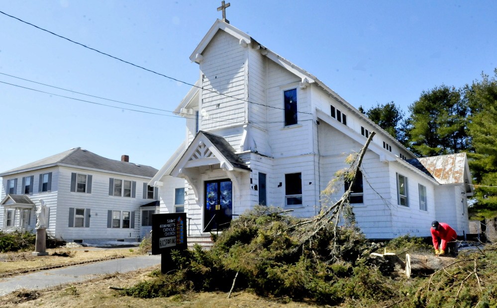 Robert Searles cuts up a tree he cut down beside St. Bridget’s church in Vassalboro on Sunday. Rachel and James Kilbride bought the closed church and rectory, left, and plan to restore the buildings and open them as an event hall and community center.