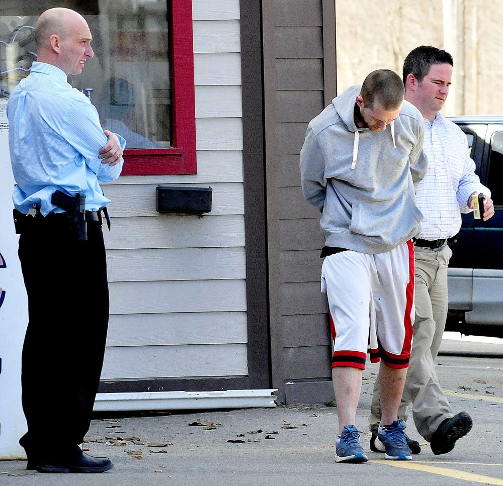 Waterville Police Detective Sgt. Bill Bonney, left, watches as Matthew Davidson, 28, of Fairfield, is led to a waiting police cruiser after his arrest outside of Jokas’ Discount Beverage on Front Street in Waterville on Tuesday.