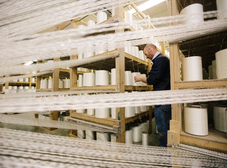 Kirk Hall checks on the fiberglass “yarn packages” feeding into an industrial loom making heat-resistant fabric at Auburn Manufacturing in Mechanic Falls. The company says having a skilled workforce to draw from is the primary factor when it’s deciding whether to create new jobs. Whitney Hayward/Staff Photographer