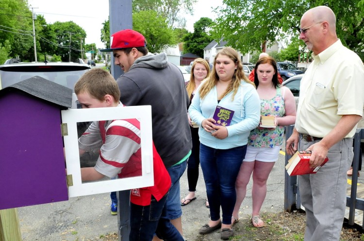 Steve Soule, right, director of the South End Teen Center in Waterville, watches on Wednesday as Logan O’Neal adds books to the Little Free Library on Water Street in Waterville while other donors await their turns. People can take books for free and are encouraged to leave books behind.