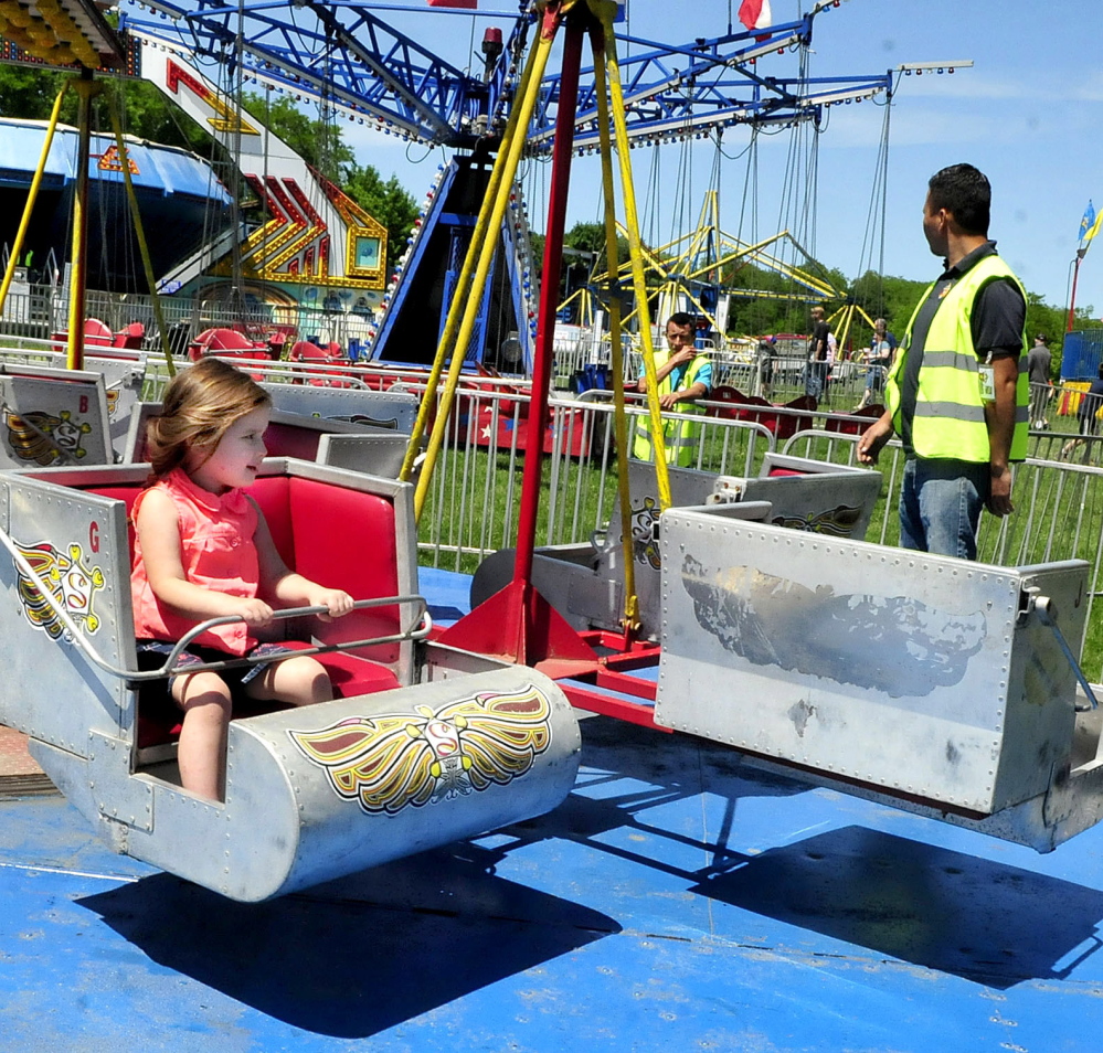 Raine Richardson enjoys a ride at the carnival in Waterville on Sunday, while a Smokey’s Greater Shows worker, at right, speaks with another worker who was waiting for customers on the Air Time swing ride, where a woman was injured on Saturday.