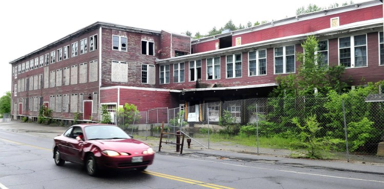 A motorist passes by the Forster Mill on Tuesday in Wilton. The town took over the mill through foreclosure last spring and is slowly moving toward demolition, helped by $25,000 approved at Town Meeting last week.