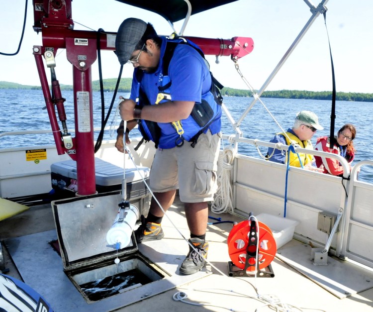 Colby College student Sergio Madrigal lowers equipment that collects water samples at desired depths in Great Pond in Belgrade on Thursday. Charlie Baeder, executive director of Belgrade Regional Conservation Association, and Lake Science Manager Brenda Fekete wait in another boat beside the research vessel.