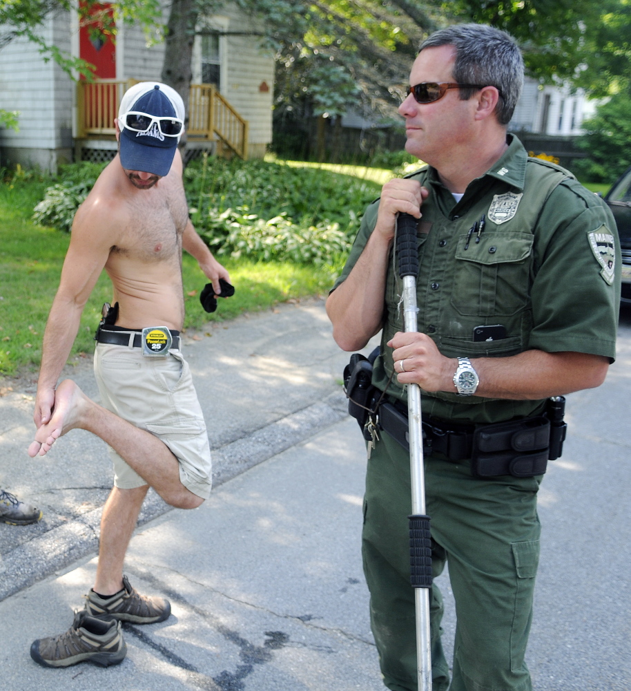 Jared Stevens inspects his foot Monday after a gray fox bit him on the steps of his Monmouth home. District Game Warden Steve Allarie searched for the animal that also bit another person. Stevens put a pistol in his waistband after the attack.