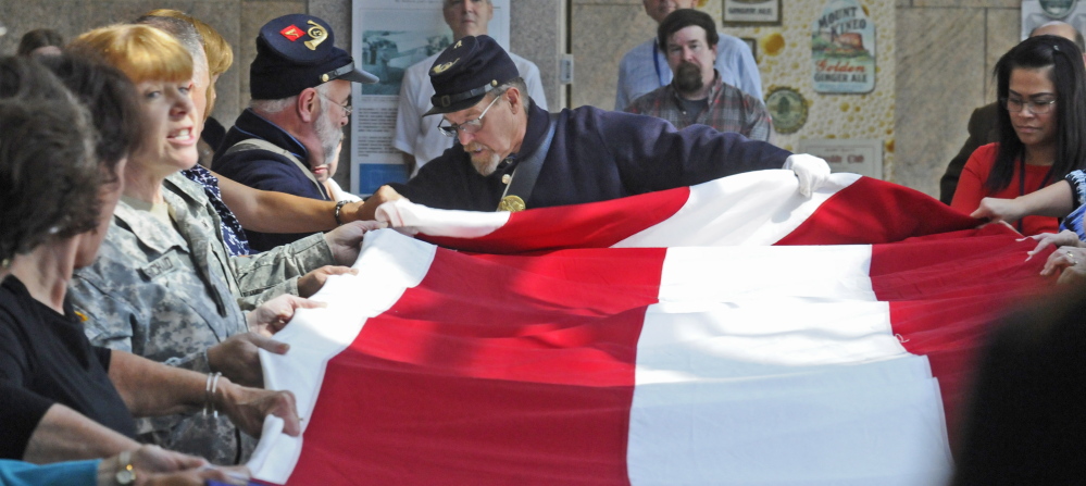 Historians and others fold an 18 by 33 foot replica of an 1860 garrison flag during a ceremony on Wednesday in the Maine State Cultural Building in the State House complex in Augusta.