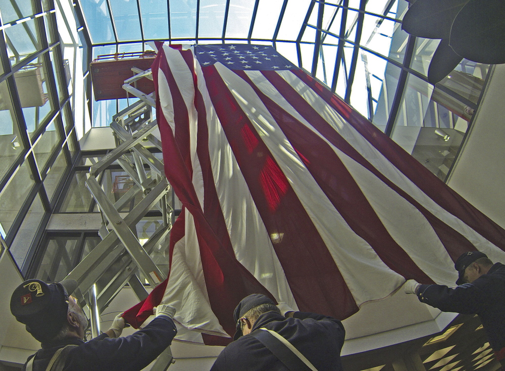 Bureau of General Services workers lower an 18 by 33 foot replica of an 1860 garrison flag down to waiting Civil War re-enactors during a flag retirement ceremony on Wednesday in the Maine State Cultural Building in the State House complex in Augusta.