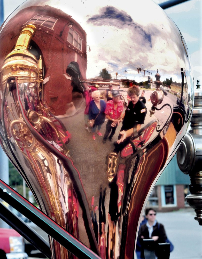 Reflected in the copper air chamber of an 1884 Button Steamer, Lt. Scott Holst, right, of the Waterville Fire department, explains how the firefighting engine worked to Arlene and Perley Roy during an open house at the Central Station on Sunday.