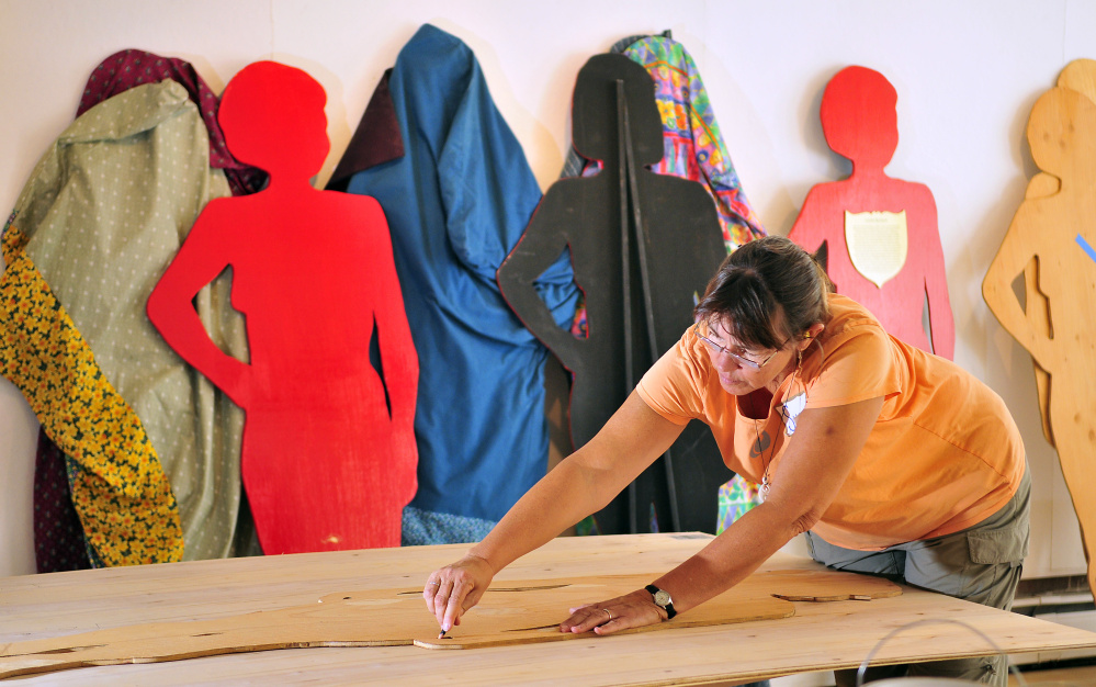 Susan Fuller traces a silhouette for another Silent Witness on a sheet of wood on Thursday at the Harlow Gallery in Hallowell.