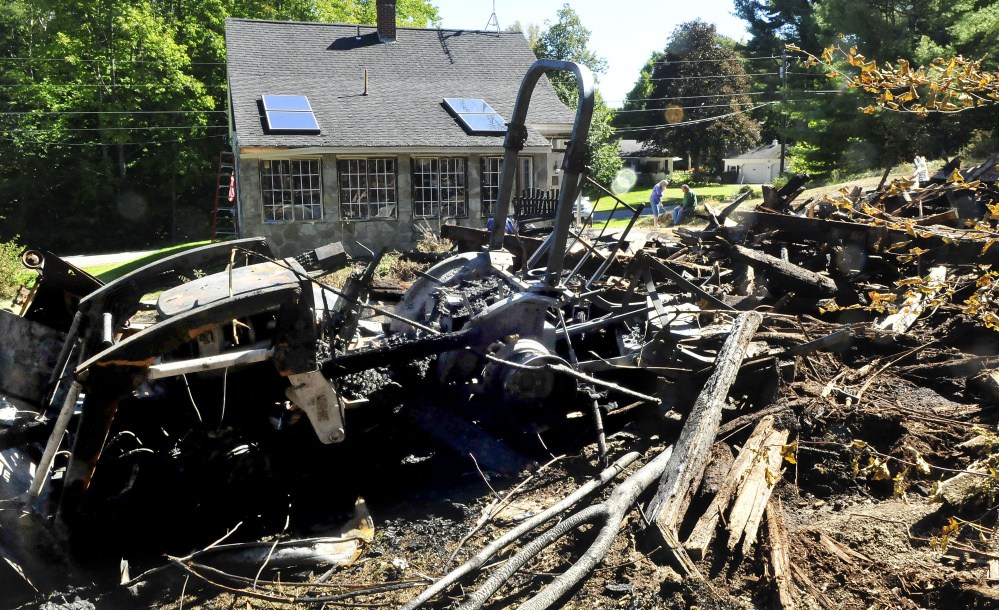 Laurie and Rick Vigue, background, take a break beside the burned remains of their barn on Sunday. Fire destroyed the 60-year-old barn and did minor damage to the Vigues’ home in Winslow. They lost a brand new tractor in the foreground.