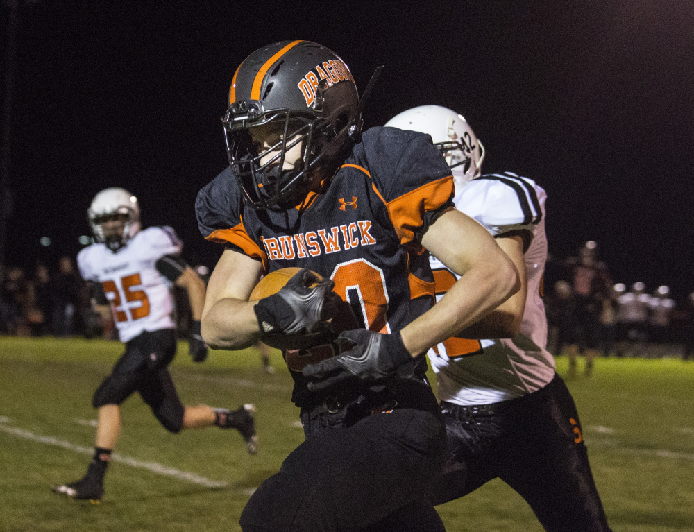 Portland Press Herald photo by Whitney Hayward 
 Brunswick running back Hunter Garrett runs past Skowhegan defensive lineman Spencer Salley, left, and Jordan Meader during a Pine Tree Conference Class B game Friday night in Brunswick.