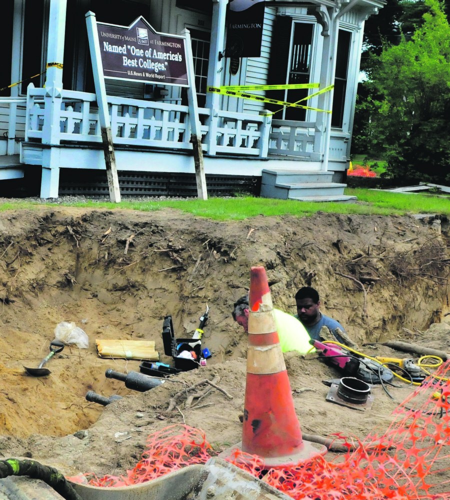 Workers install pipe for the biomass heating system beside a University of Maine at Farmington building.