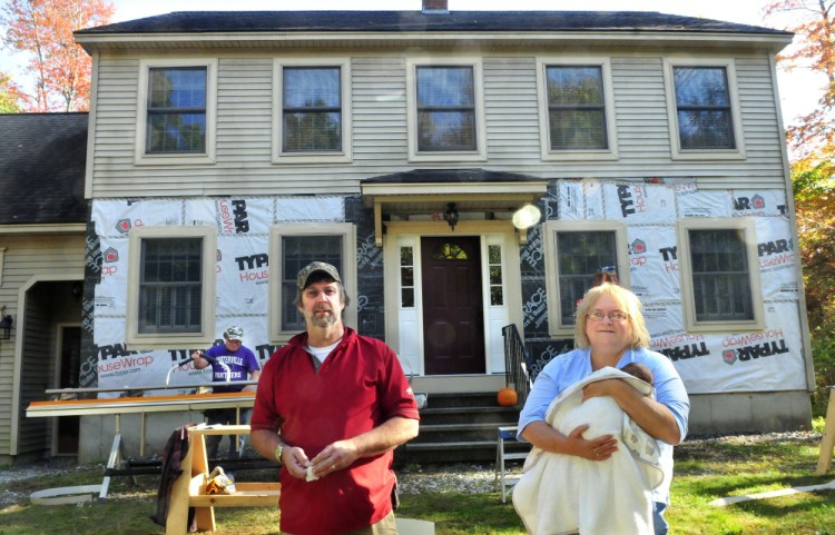 Chris and Janet Weeks stand outside their Oakland home on Monday after volunteers, including Brian Jacques, background, helped repair their home that had serious damage in the walls from leaking water.