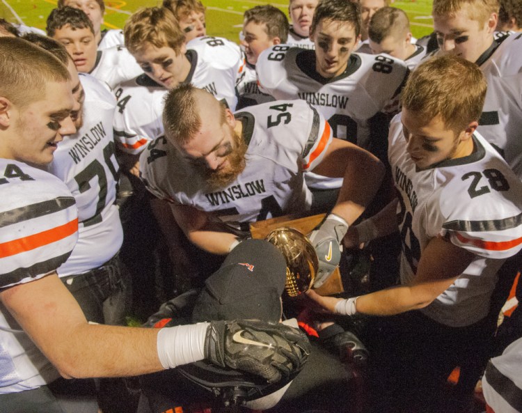 Members of the Winslow football team hold the Gold Ball for former coach Jim Poulin to kiss after they won the Class C championship Saturday at Fitzpatrick Stadium in Portland.