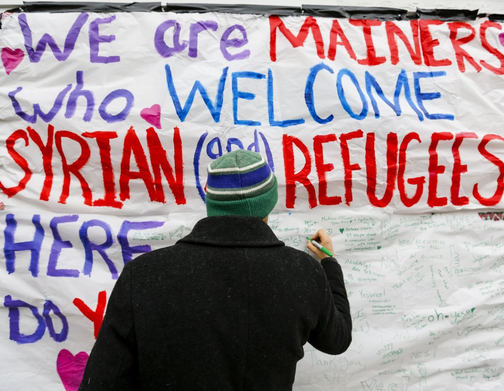 Munjoy Hill resident David Benson adds a message of support to a sign on Congress Street calling for a welcoming attitude toward the prospect of Syrian refugees.