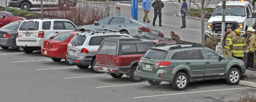A tow truck operator, center, starts to work at removing the gray Buick that collided with seven parked cars on Friday in front of MaineGeneral Medical Center in Augusta.
