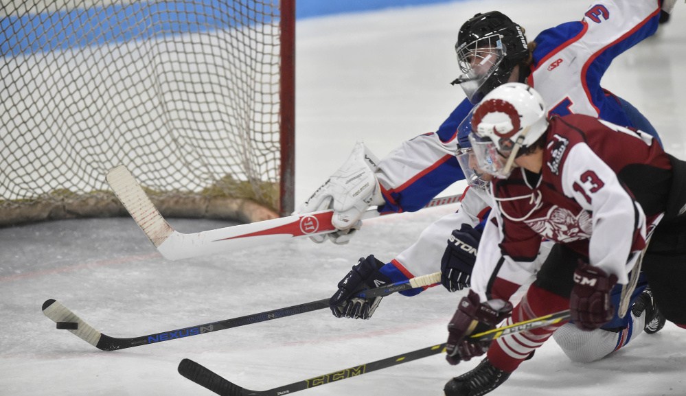 Messalonskee High School’s Connor Smith (5) center, gets his stick on the puck to deflect a shot by Bangor High School’s Cameron Burpee (13) right, as Messalonskee goalie Eli Michaud (33) stretches for the save in the second period Saturday at Sukee Arena in Winslow.