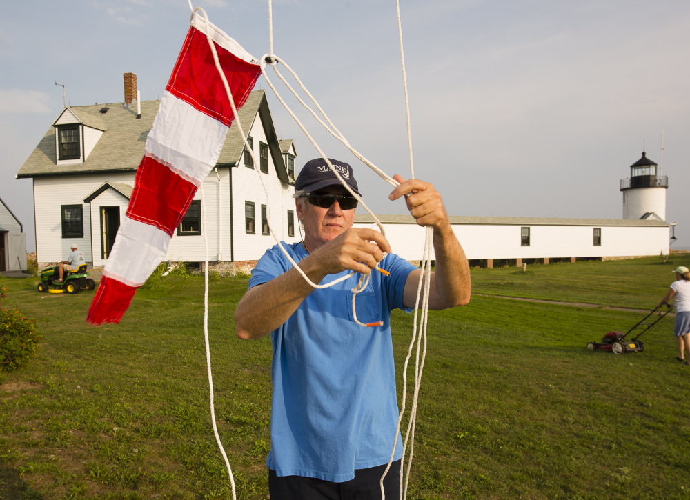 Kennebunkport Conservation Trust volunteer Gregg Maynard of Kennebunkport and Texas raises colors on the flag pole during a volunteer work session to maintain the trust’s property off Cape Porpoise. Volunteers Russ and Julie Grady of Kennebunkport cut the lawn in the background.