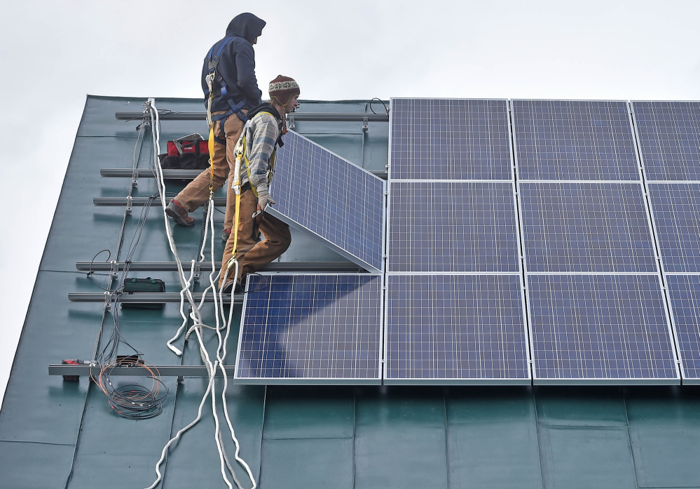 Ben Holt, foreground, and Jake Hunt, back, install a solar panel Tuesday on the Vassalboro Friends Meeting building in Vassalboro.