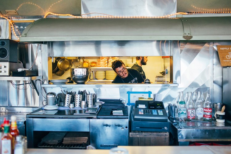 Palace Diner co-owner Greg Mitchell peers into the dining area, while co-owner Chad Conley walks by in the kitchen. Eater.com's restaurant editor says Conley and Mitchell "have recalibrated greasy spoon staples , , ,  without losing the everyman appeal."