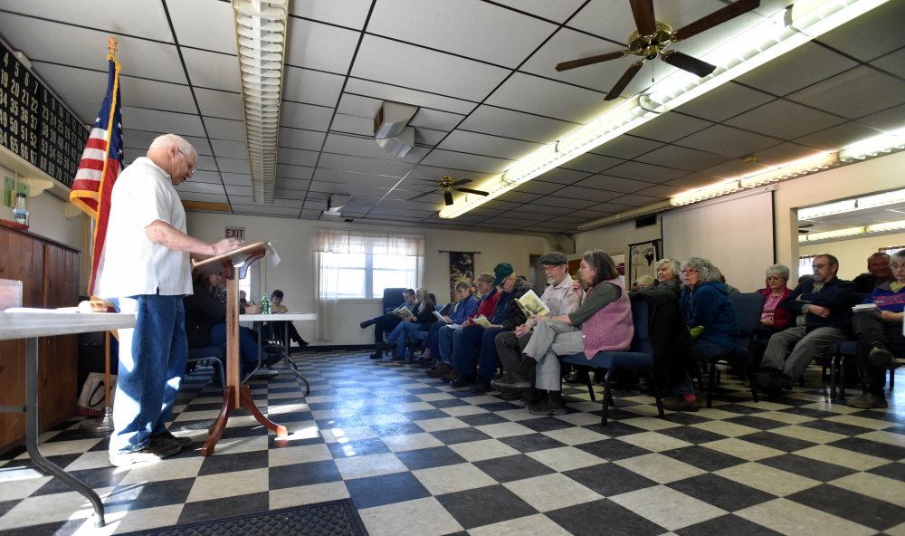 Marc Courtemanche, left, stands at a lectern to moderate the Athens Town Meeting on Saturday during a vote at the Town Office.