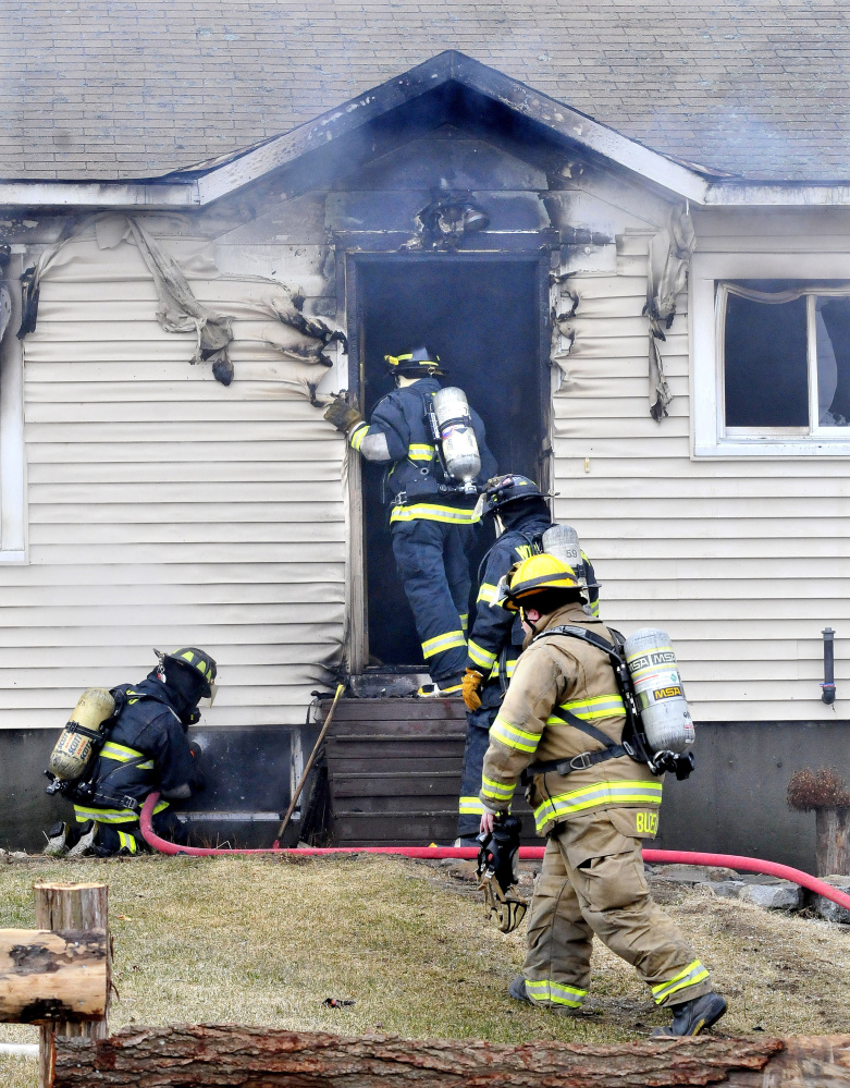 Firefighters enter the burned-out front entry to a home at 668 Village Road in Smithfield Thursday.