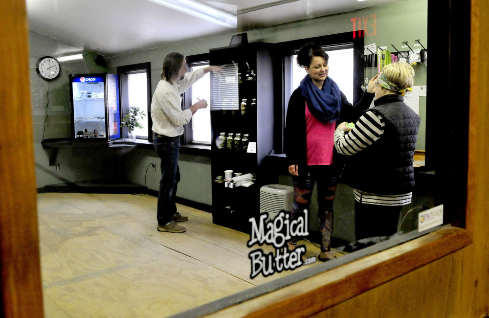 Inside the product room, where only medical marijuana prescription holders may enter, owner Dawson Julia arranges varieties of marijuana grown and sold at his East Coast CBDs business Thursday in Unity. His wife, Kelly, center, and his mother, Ginger Muradian, speak at right.