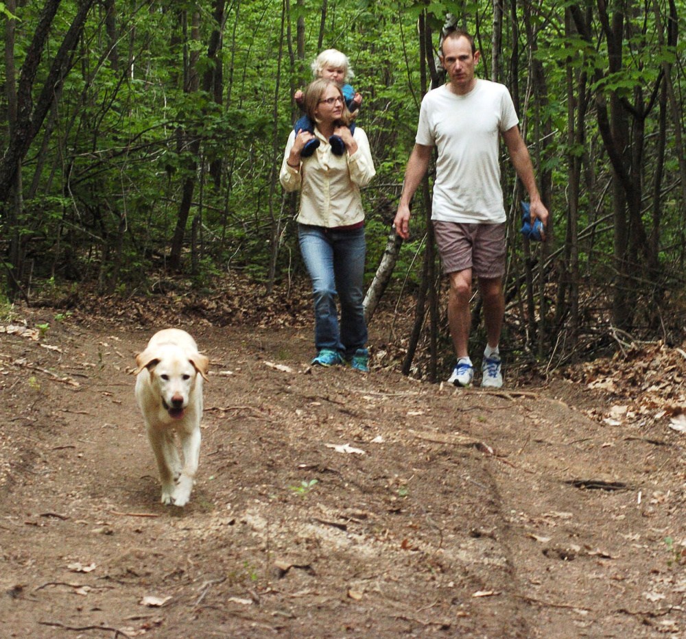 Lyra and Marc Collard and their daughter Ara and dog Sunny walk along a trail Tuesday at their Wilder Hill Trails in Norridgewock. The couple are opening free public-access walking and running trails on their property with a New Balance Move More Kids grant.