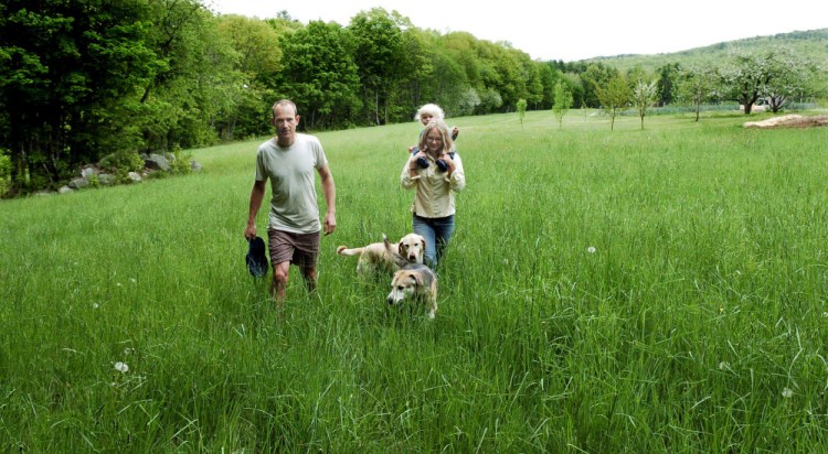 Marc and Lyra Collard, daughter Ara and dogs walk in a field Tuesday in Norridgework, where they are establishing the Wilder Hill Trails. The couple are opening the free public-access walking and running trails on their property with help from a New Balance Move More Kids grant.