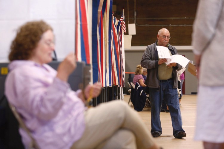 Thomas Yarborough exits the voting booth with his ballots Tuesday at the Saco Community Center as Ward 5 poll worker Margaret Mills tends the electronic ballot box.