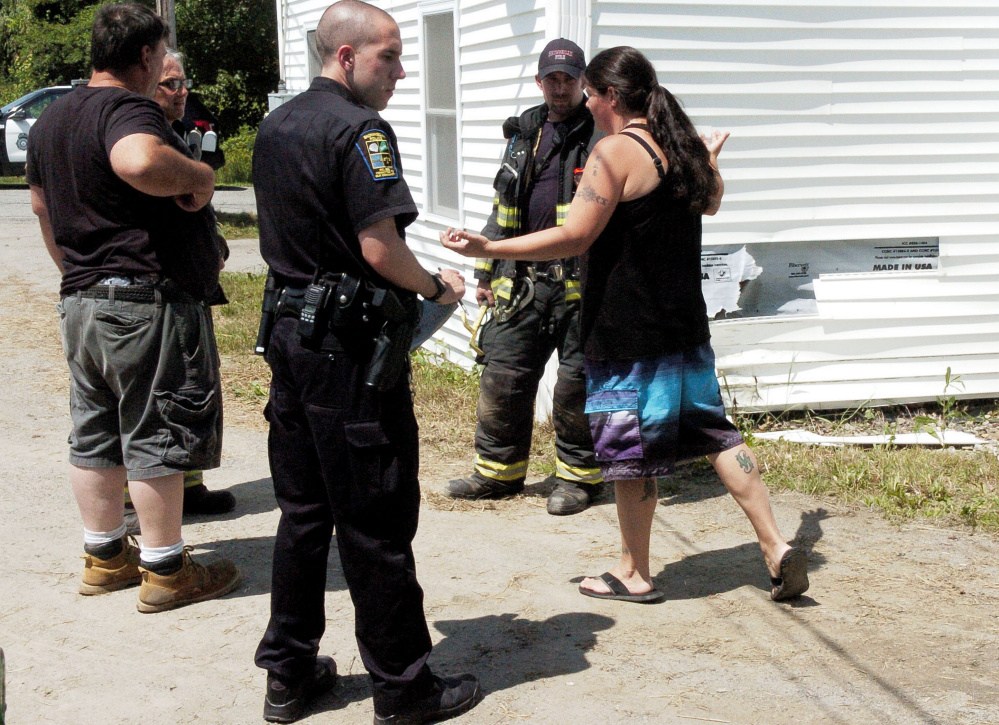 Skowhegan Police Officer Michael Bachelder and firefighters listen to witnesses next to the crash site where an SUV struck the corner of a home off Dartmouth Street in Skowhegan on Tuesday.