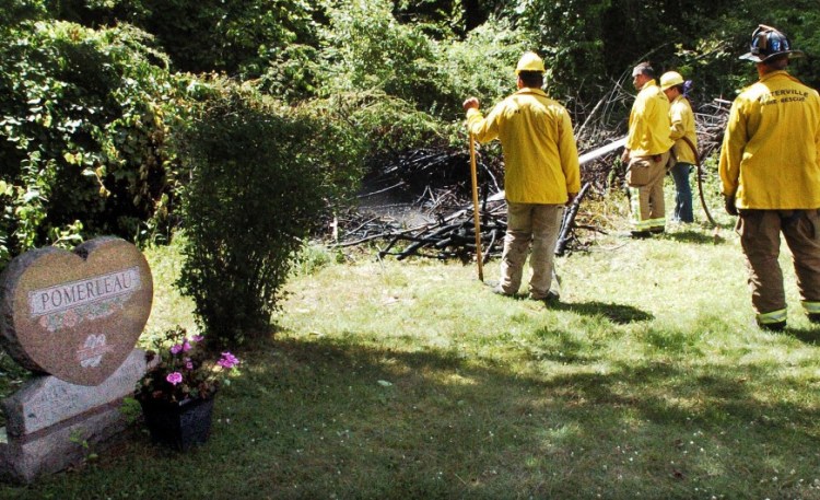 Waterville firefighters extinguish fire in some brush July 21 beside gravesites at St. Francis Catholic Cemetery in Waterville. Police have charged a city man in connection with setting a pair of fires at the St. Francis and Pine Grove cemeteries that day.