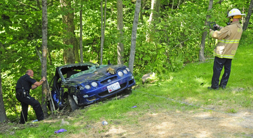 Augusta police Officer Donald Whitten, left, and Augusta Fire Department Battalion Chief Steve Leach photograph the wreckage of a 2001 Hyundai on Saturday during investigation of the car's crash on Bond Brook Road in Augusta. The crash injured four people.