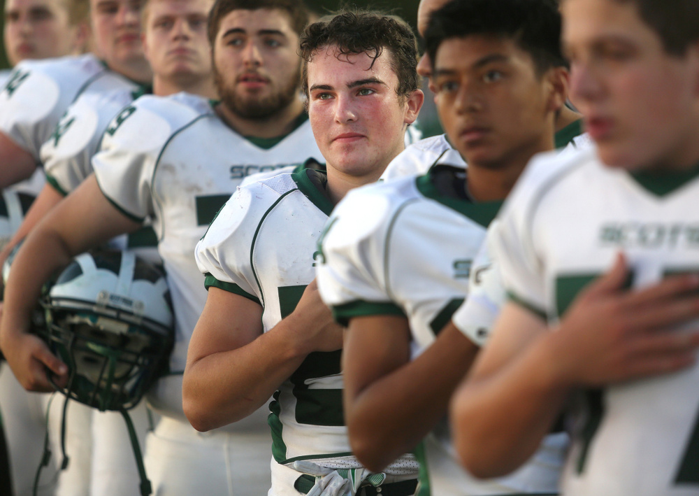 Football players from Bonny Eagle High School stand for the national anthem before their game against Scarborough on Friday night. A state organization has warned schools to prepare for possible protests during the national anthem.