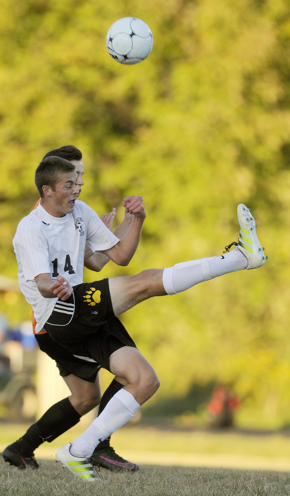 Maranacook's Hayden Elwell, left, kicks the ball behind himself and Winslow's Jake Warn during a game Thursday in Readfield.