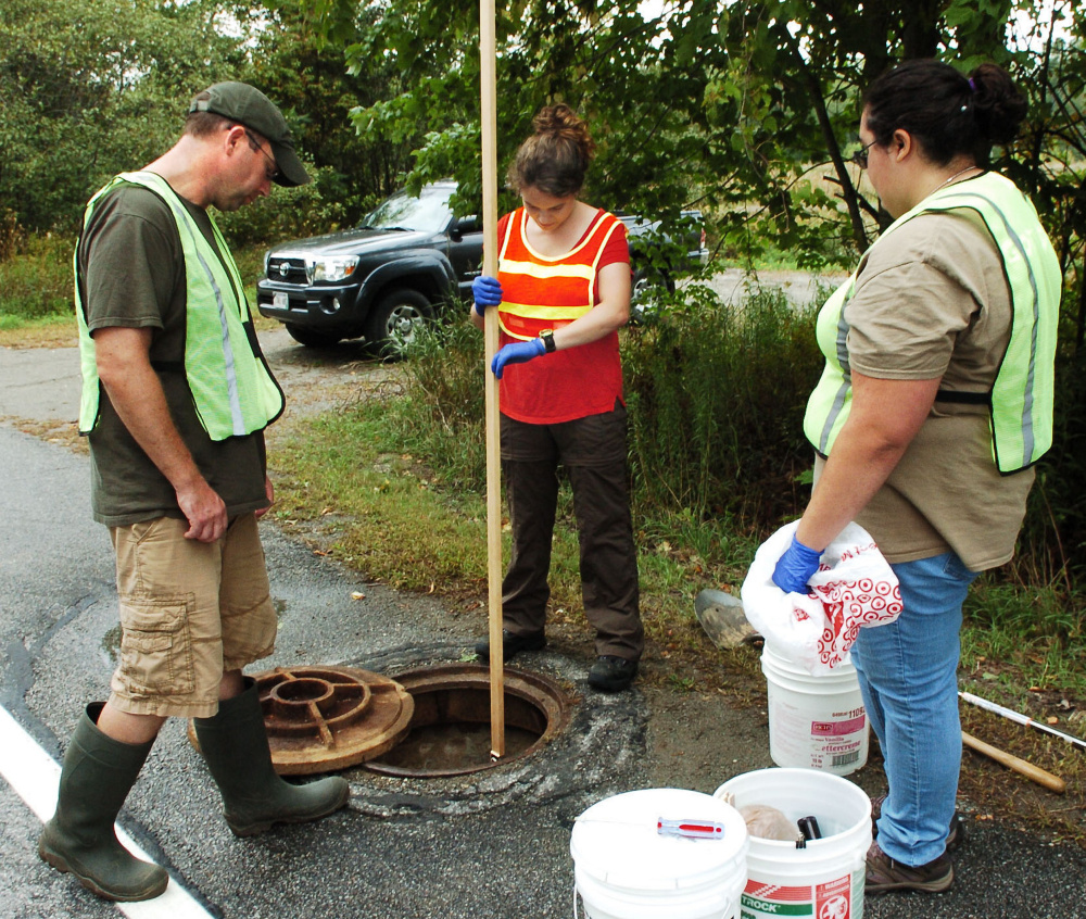 Kevin Spigel, left, Unity College professor and president of the Unity Utilities District, watches as students Sally Carullo, center, and Alyssa Silvia take measurements of the depth of wastewater running in a pipe from the campus on Monday.